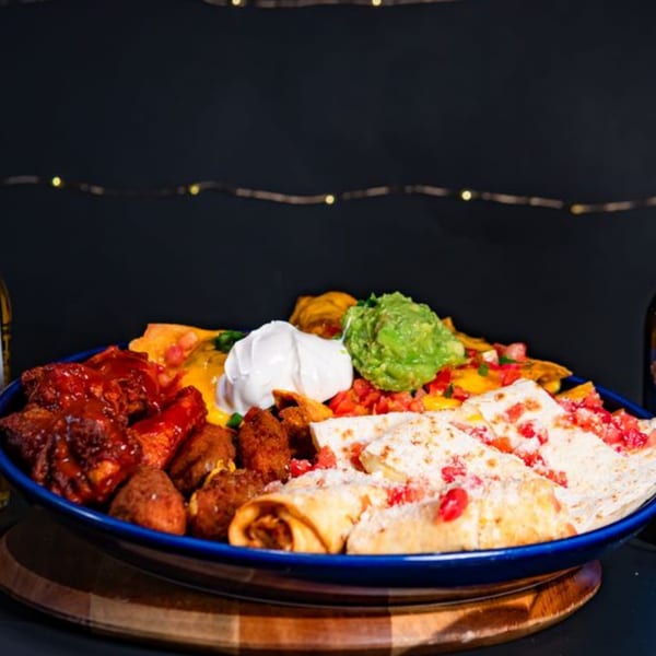 A large blue platter of Mexican appetizers including nachos, quesadillas, taquitos, and chicken wings.