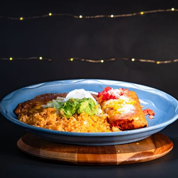 A Mexican combination plate with a burrito, rice, refried beans, guacamole, and sour cream.