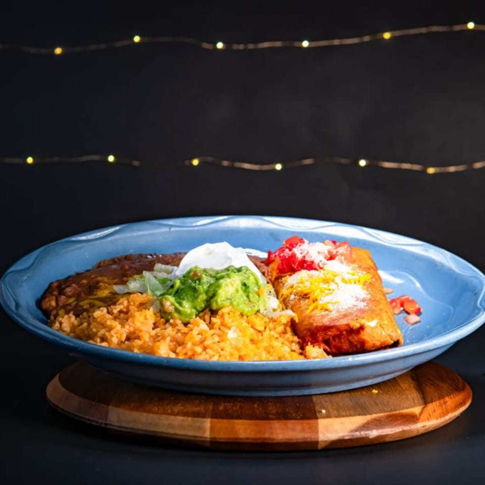 A Mexican combination plate with a burrito, rice, refried beans, guacamole, and sour cream.