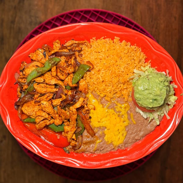 Chicken fajitas with rice, refried beans, guacamole, and shredded lettuce on a red plate.
