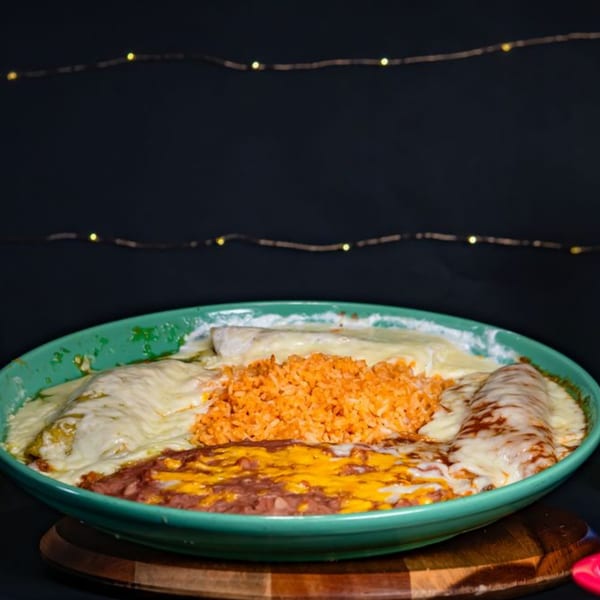 A large platter of Mexican food with enchiladas, rice, and refried beans, all covered in cheese.